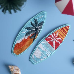 Op de afbeelding: Twee geborduurde surfplankpatches met tropische ontwerpen. E&eacute;n heeft een palmboom over een oranje en geel strand, de andere een rode en gele zonsondergang met een palmboom. De patches zijn lichtblauw omlijnd.