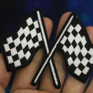 以下が含まれることがあります： 黒と白の市松模様のレーシングフラッグが2つ、交差しています。フラッグは白いステッチで刺繍されています。