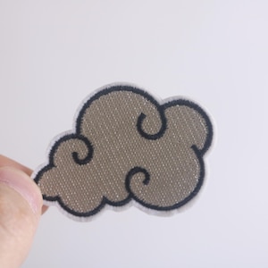 May include: A brown and black embroidered cloud patch. The cloud is stylized with a swirling design.