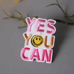 May include: Pink and gold embroidered iron-on patch with the text "YES YOU CAN" and a yellow smiley face.