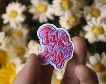 Könnte beinhalten: Rosa und blaue gestickte Bügel-Applikation mit dem Text "Take it Easy".