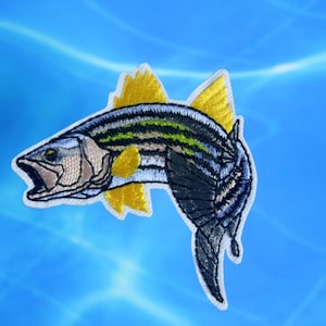 Op de afbeelding: Gestikte patch van een gestreepte zeebaars met gele vinnen, die uit het water springt. De vis is gedetailleerd met zwarte, witte en groene strepen.