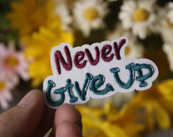 Könnte beinhalten: Weißer gestickter Aufnäher mit den Worten "Never Give Up" in türkisfarbener und burgunderroter Schrift.