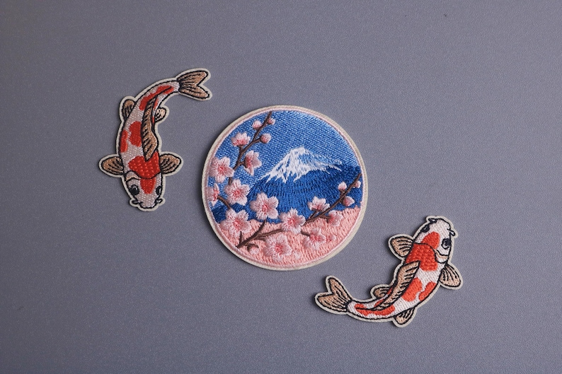 May include: Embroidered patches featuring Japanese motifs. Includes two koi fish patches in red, white, and brown, and a circular patch with Mount Fuji, cherry blossoms, and a blue sky background.