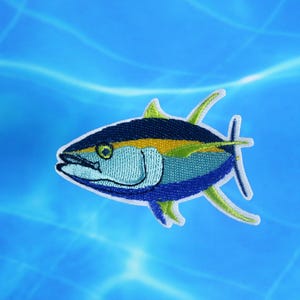 May include: Embroidered patch of a blue and yellow tuna fish with green fins, against a blue background.