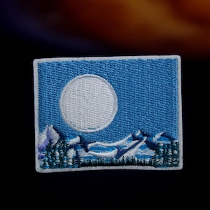 Peut inclure: Un patch brodé bleu avec une lune blanche et une chaîne de montagnes blanche au premier plan. Le patch est entouré d'une bordure blanche.