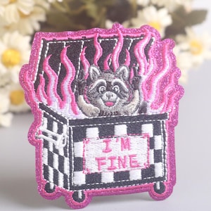 Puede incluir: Parche bordado con un mapache en un contenedor de basura envuelto en llamas rosas. El contenedor tiene un patrón de cuadros blancos y negros y el texto "I'M FINE" en rosa. El parche tiene un borde rosa brillante.