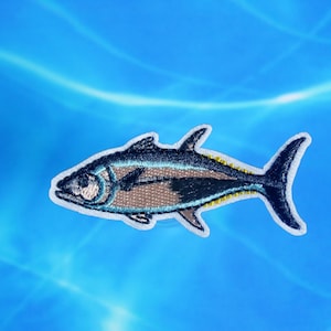 May include: Embroidered iron-on patch of a blue and silver fish with yellow accents. The fish is swimming to the right.
