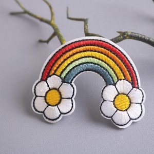 May include: Embroidered rainbow patch with white daisy flowers on each side. The rainbow has red, orange, yellow, green, blue, indigo, and violet stripes.