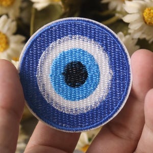 Könnte beinhalten: Ein blauer und weißer gestickter Augen-Patch mit einem weißen Kreis und einer blauen Mitte. Der Augen-Patch ist ein beliebtes Symbol für Schutz und Glück.