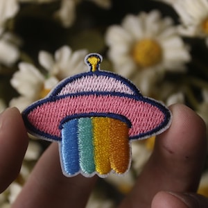 May include: A pink and blue embroidered UFO patch with a rainbow stripe design.