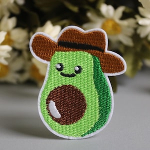 Pode incluir: Patch bordado com um abacate sorridente usando um chapéu de cowboy marrom. O abacate é verde com um caroço marrom e realces brancos, delineado com costura branca. Para roupas ou acessórios.