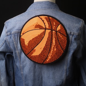 Op de afbeelding: Een spijkerjack met een oranje en zwarte basketbal patch op de rug.