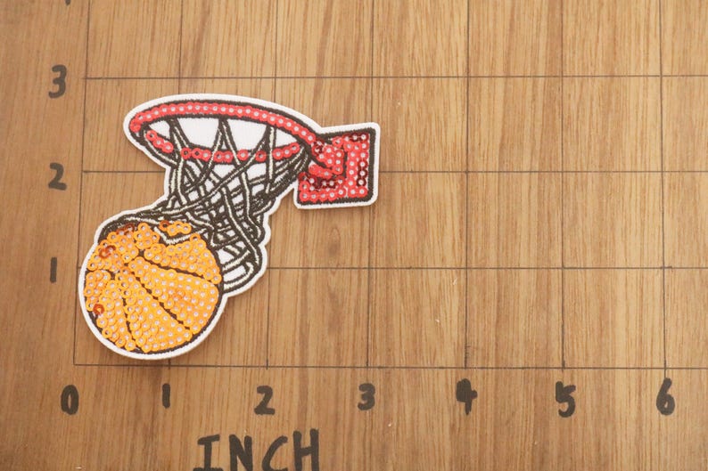 Peut inclure: Un &eacute;cusson de basket-ball repr&eacute;sentant un ballon de basket-ball traversant un filet. Le ballon est orange avec des lignes noires, et le filet est blanc et noir. Le cercle est rouge avec des points blancs. L'&eacute;cusson mesure environ 5 cm de large.