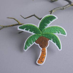 Peut inclure: Patch brodé représentant un palmier vert avec une noix de coco brune et un tronc orange.