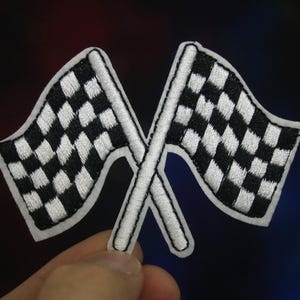 May include: Two white and black chequered racing flags crossed over each other. The flags are embroidered and have a white outline.