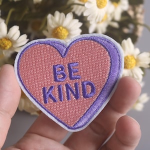 May include: Purple heart-shaped embroidered patch with the words "Be Kind" in pink thread.