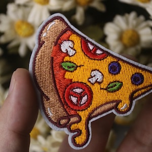 May include: A yellow and brown embroidered pizza slice patch with red tomato, white mushroom, green pepper, and blue blueberry toppings.