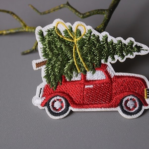 Könnte beinhalten: Rote bestickte Auto, das einen grünen Weihnachtsbaum mit einer gelben Schleife oben trägt.