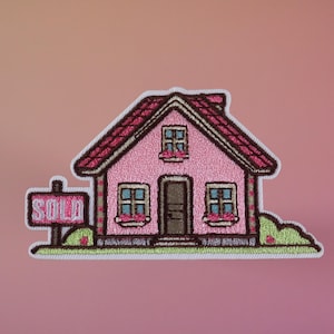 May include: A pink house with a red roof and white trim. The house has two windows and a door. There is a sign in front of the house that says "SOLD".