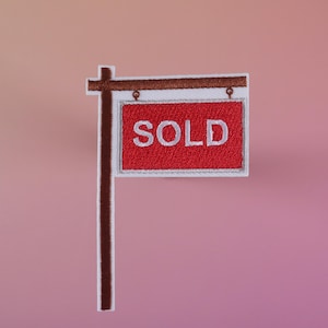May include: A red and white sign with the word "SOLD" on it, hanging from a brown wooden post.