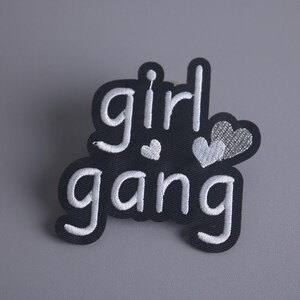 May include: Black iron-on patch with white embroidery that reads "girl gang" with two white hearts.