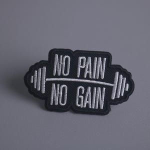 Puede incluir: Parche bordado en blanco y negro con una barra de pesas y el texto "NO PAIN NO GAIN".