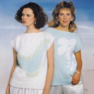 May include: Two women wearing knitted tops. One top is white with a blue and green design, the other is light blue with a white floral pattern. Both tops have short sleeves and a boat neck. The background is a gradient of blue and white.