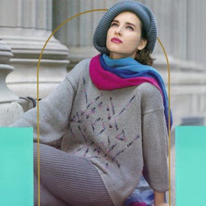 Può includere: Un maglione grigio chiaro con un design geometrico rosa e viola, abbinato a leggings grigi. L'outfit è completato da un basco blu e una vivace sciarpa rosa e blu. L'aspetto generale è casual e alla moda.