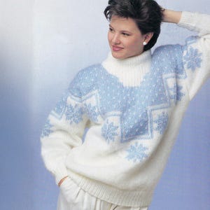 May include: A white and light blue knitted jumper with a roll neck. The jumper has a snowflake design in light blue across the chest and sleeves. The sleeves are long and the jumper is a loose fit.