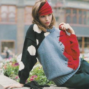 May include: A color-blocked sweater featuring a black sleeve with white polka dots and a light blue body with a red accent. The sweater is paired with a red headband. Black gloves are visible.