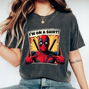 May include: A black t-shirt featuring a comic book style graphic of Deadpool pointing at himself and saying "I'm on a shirt!"