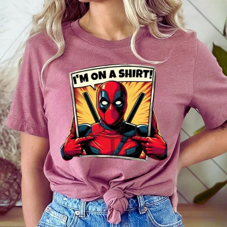 May include: A pink t-shirt featuring a comic book style graphic of Deadpool in a frame. The text "I'M ON A SHIRT!" is in a speech bubble above Deadpool.