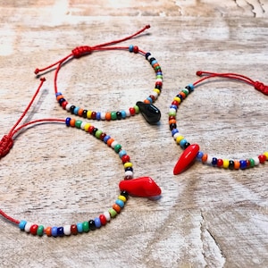 May include: Three red string bracelets with colourful glass beads and red glass charms. The charms are shaped like chilli peppers.