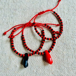 May include: Two red and black beaded bracelets with red string ties. One bracelet has a black and red pendant and the other has a red pendant.