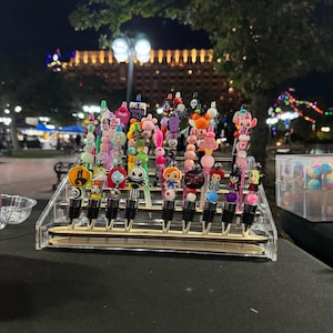 May include: A display of colorful bottle stoppers with various Halloween-themed characters and designs. The stoppers are arranged on a clear acrylic stand.