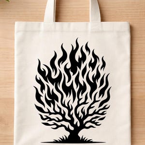 May include: Cream-colored tote bag featuring a black graphic of a tree engulfed in flames. The tree design has intricate branches and a fiery crown. The bag has two cream-colored handles for carrying.