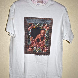 May include: White t-shirt with a graphic print of a man with multiple faces surrounding him. The graphic is in a stained glass style with a brick background. The text "INTO THE ABYSS II - © RMPROCUCTIONS" is printed below the graphic.