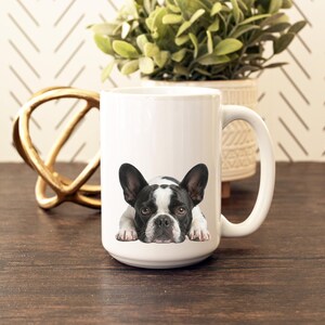 Op de afbeelding: Witte keramische mok met een zwart-witte Franse Bulldog illustratie. De hond ligt met zijn poten zichtbaar. De mok heeft een grote handgreep en staat tegen een neutrale achtergrond.