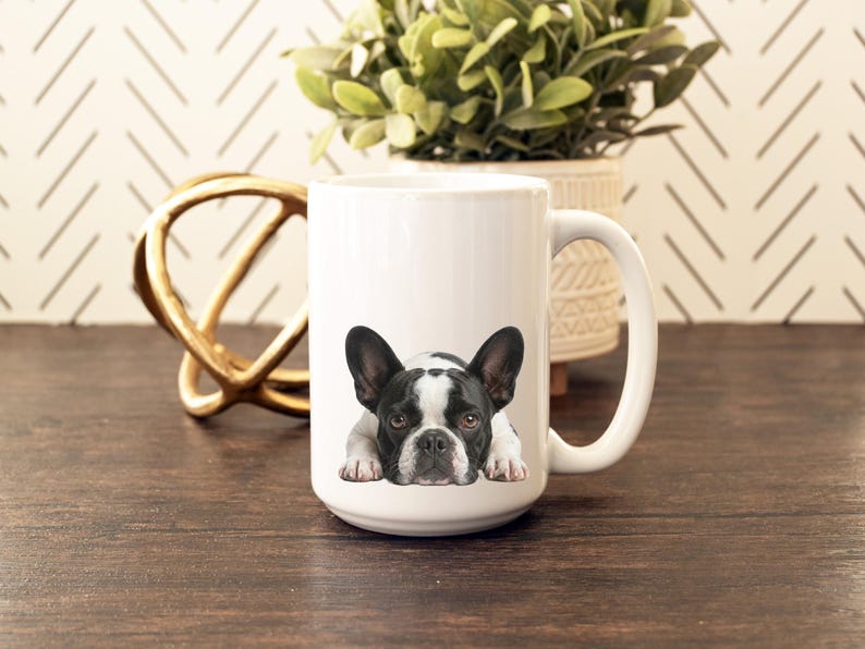 Op de afbeelding: Witte keramische mok met een zwart-witte Franse Bulldog illustratie. De hond ligt met zijn poten zichtbaar. De mok heeft een grote handgreep en staat tegen een neutrale achtergrond.