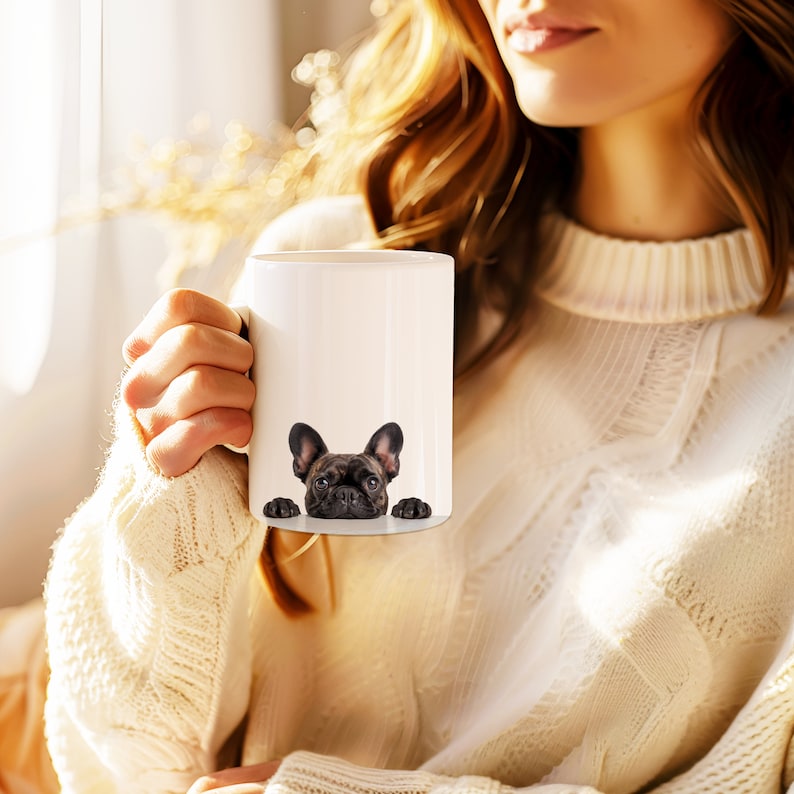 May include: A white ceramic mug with a black French bulldog peeking over the rim. The dog has black eyes and a black nose.