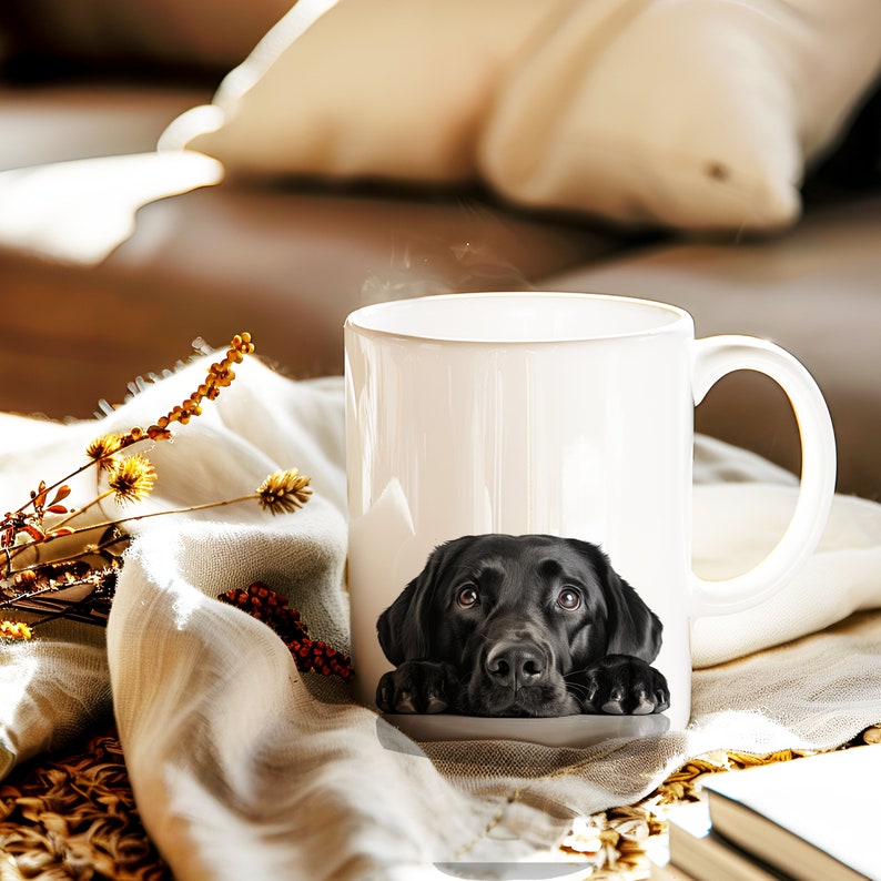 May include: A white ceramic mug with a black Labrador Retriever peeking out from the top. The dog's eyes are visible and it is looking up at the camera.