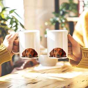 May include: Two white ceramic mugs with a dachshund dog peeking out from behind the rim of each mug. The dachshund is brown and tan with a black nose.