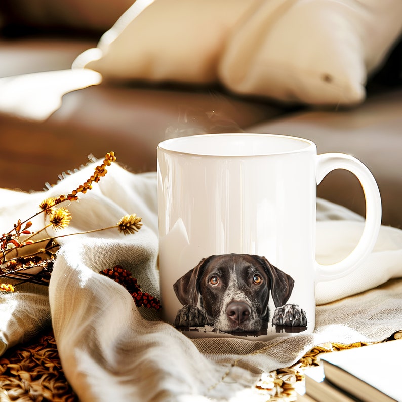 May include: White ceramic mug with a brown and white dog peeking out from the top. The dog has brown eyes and a black nose.
