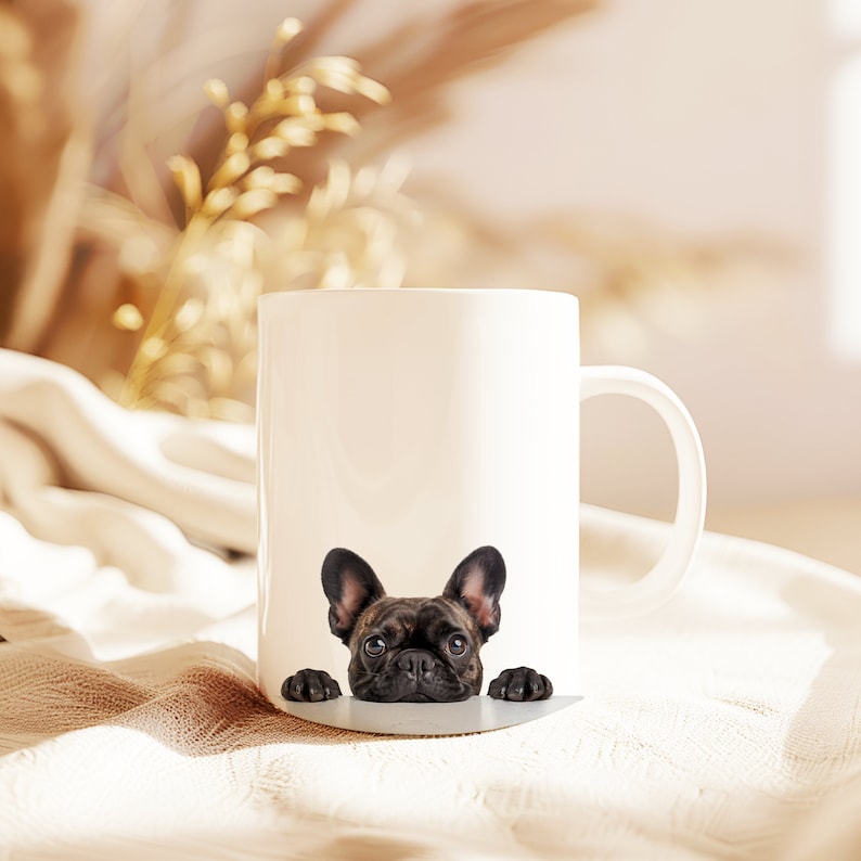 May include: White ceramic mug with a black French bulldog peeking over the rim. The dog has brown eyes and a black nose.