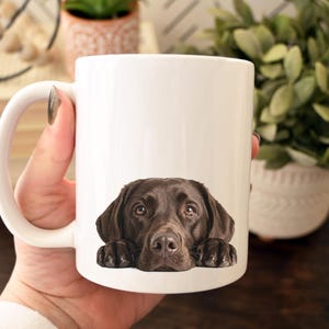 May include: White ceramic coffee mug featuring a brown Labrador Retriever dog. The dog's head and paws are printed on the mug, creating a charming and heartwarming design. Perfect for dog lovers.