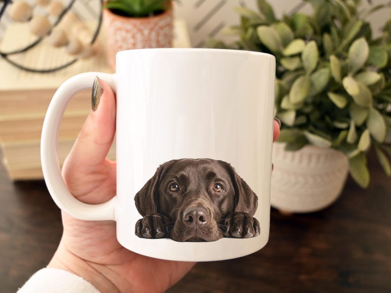 May include: White ceramic coffee mug featuring a brown Labrador Retriever dog. The dog's head and paws are printed on the mug, creating a charming and heartwarming design. Perfect for dog lovers.
