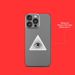 Op de afbeelding: Een grijze iPhone 13 Pro Max met een witte sticker van een alziend oog op de achterkant. Getoond op: iPhone 13 Pro Max. Getoonde grootte: 2"