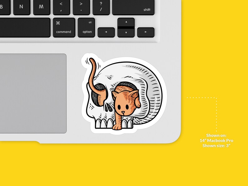 K&ouml;nnte beinhalten: Ein Aufkleber mit einem wei&szlig;en Sch&auml;del, aus dem ein kleines orangefarbenes K&auml;tzchen herausschaut. Der Aufkleber ist auf einem 14-Zoll-Macbook Pro-Laptop zu sehen.