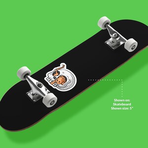 K&ouml;nnte beinhalten: Schwarzes Skateboard mit einem wei&szlig;en und orangefarbenen Totenkopf-Motiv. Gezeigt auf: Skateboard. Gezeigte Gr&ouml;&szlig;e: 5"